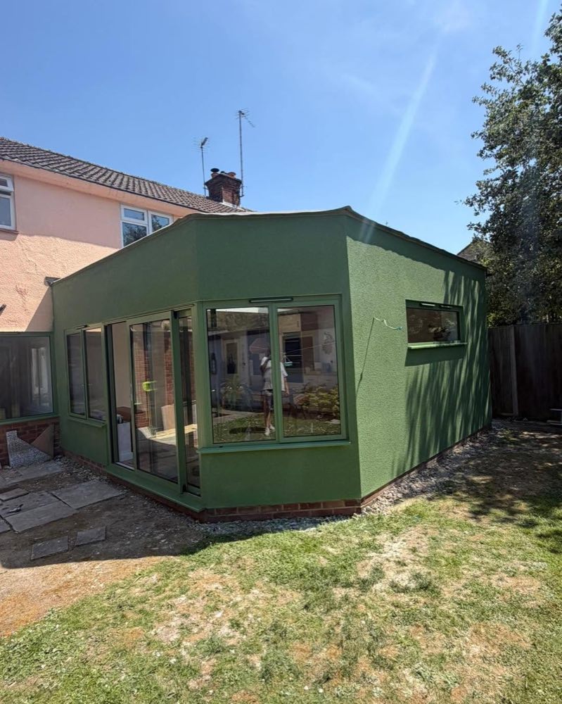 An extension finished in green silicone render, whole building in frame against a blue sky